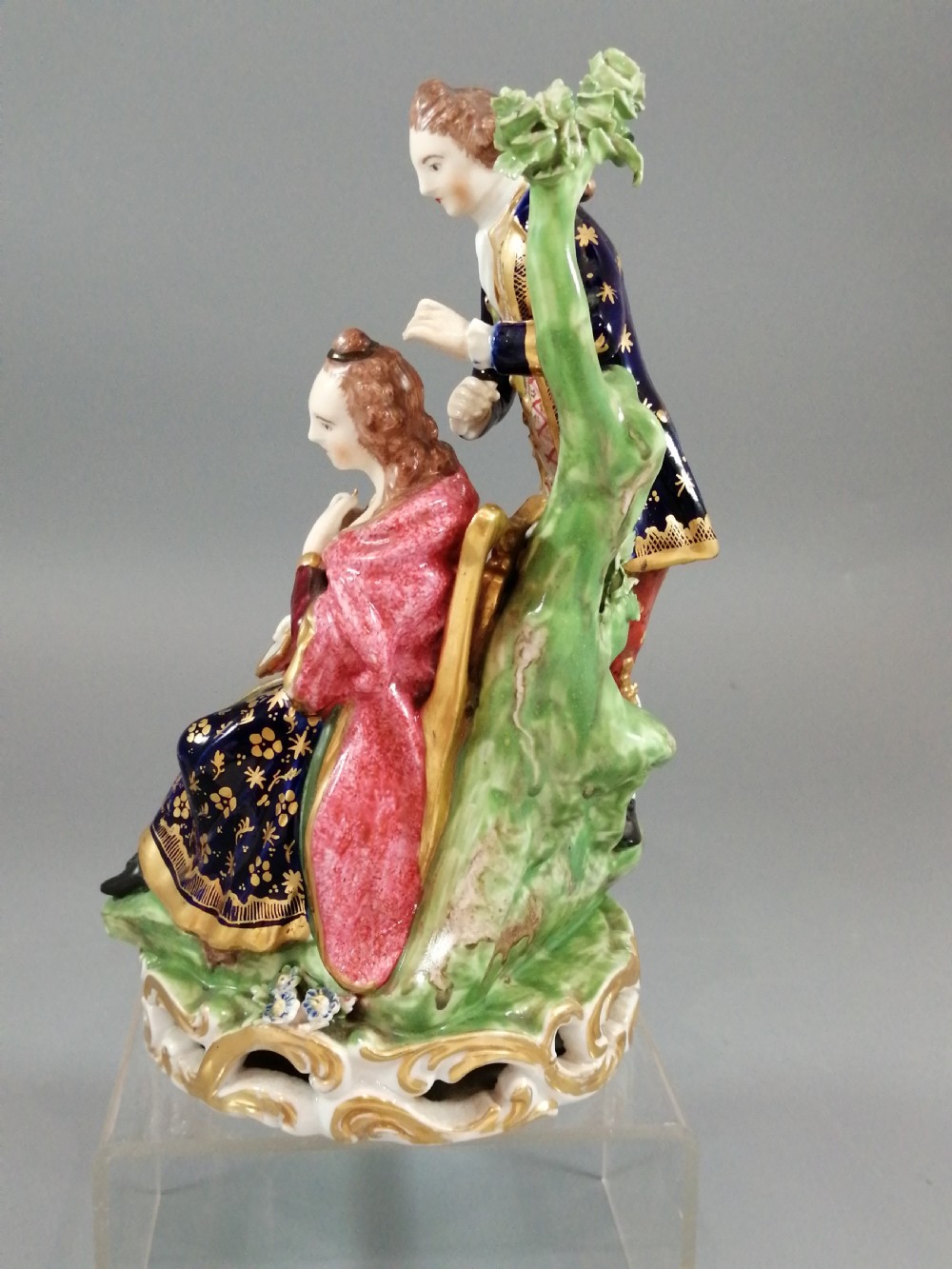 An early nineteenth-century painted porcelain figurine depicting a male court hairdresser styling a seated ladys hair on a rococo scroll base. View III