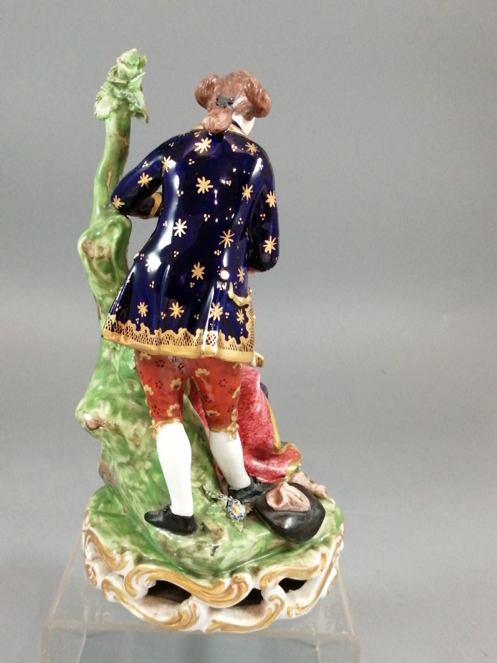 An early nineteenth-century painted porcelain figurine depicting a male court hairdresser styling a seated ladys hair on a rococo scroll base. View V