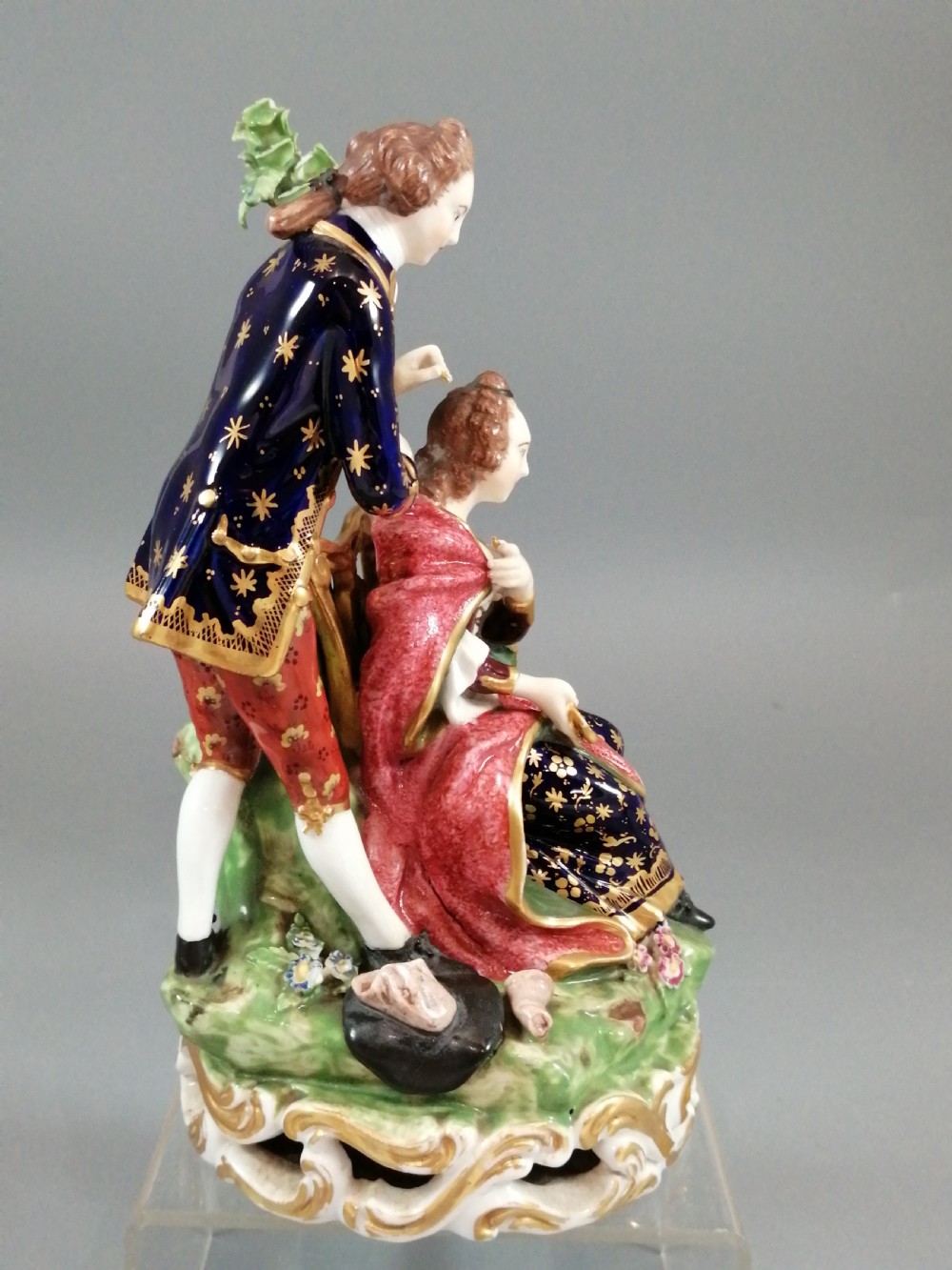 An early nineteenth-century painted porcelain figurine depicting a male court hairdresser styling a seated ladys hair on a rococo scroll base. View VI
