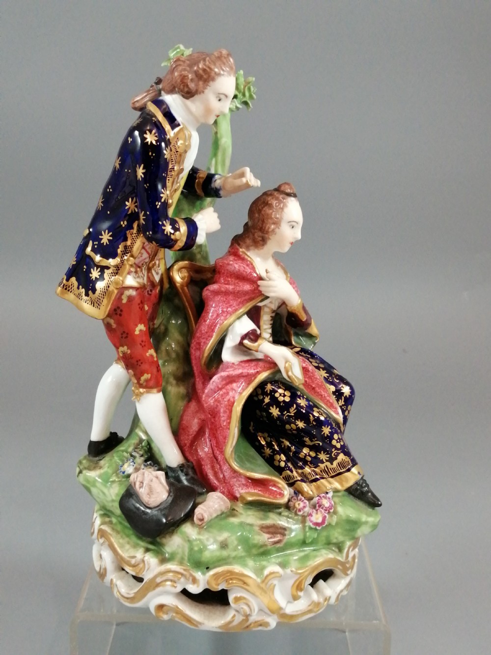 An early nineteenth-century painted porcelain figurine depicting a male court hairdresser styling a seated ladys hair on a rococo scroll base. View VII
