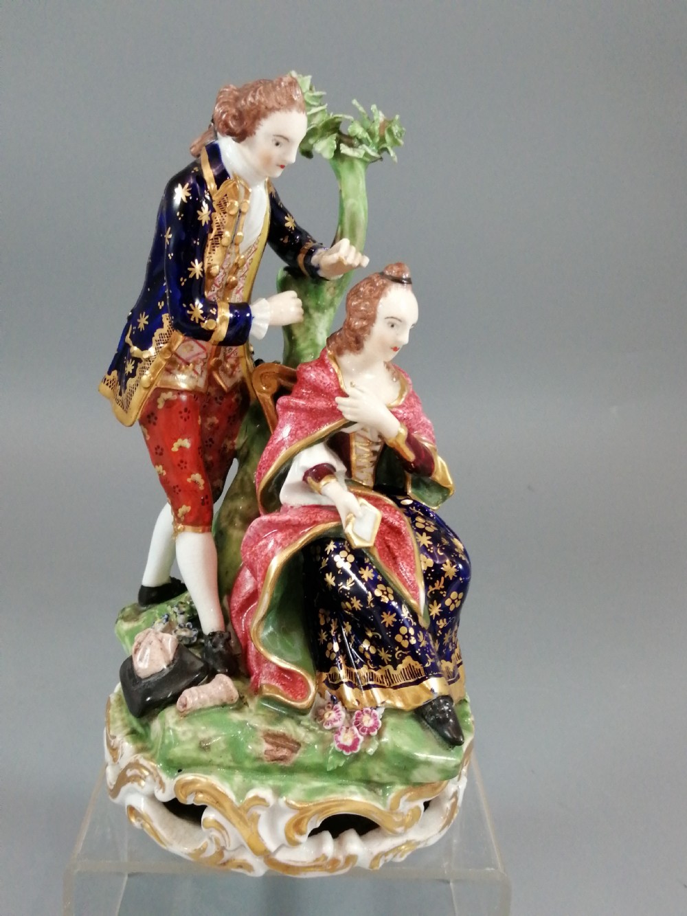 An early nineteenth-century painted porcelain figurine depicting a male court hairdresser styling a seated ladys hair on a rococo scroll base. View VIII