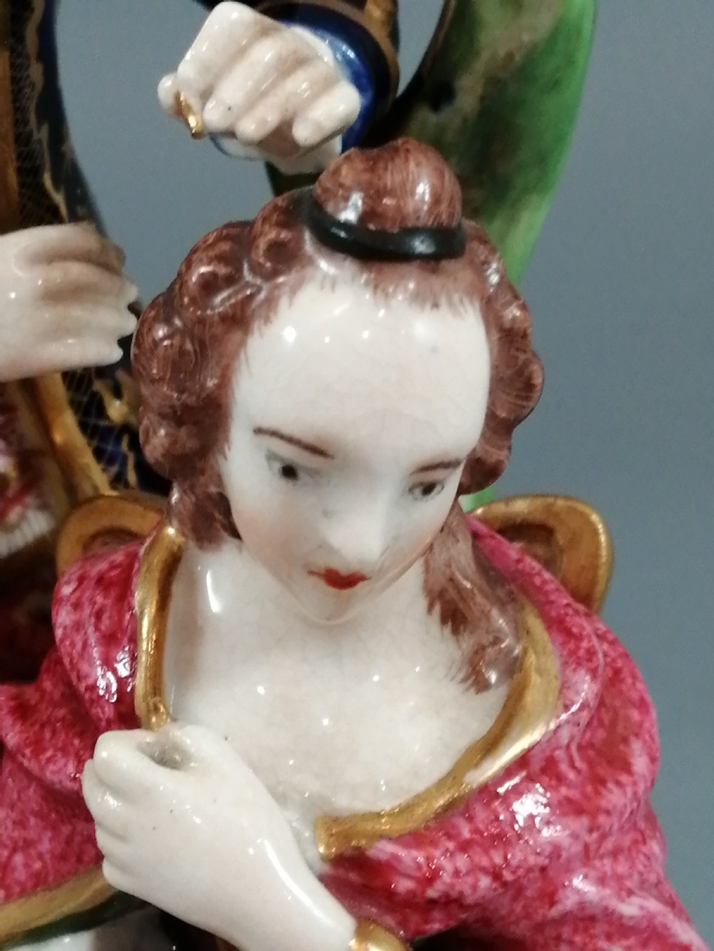 An early nineteenth-century painted porcelain figurine depicting a male court hairdresser styling a seated ladys hair on a rococo scroll base. View XII
