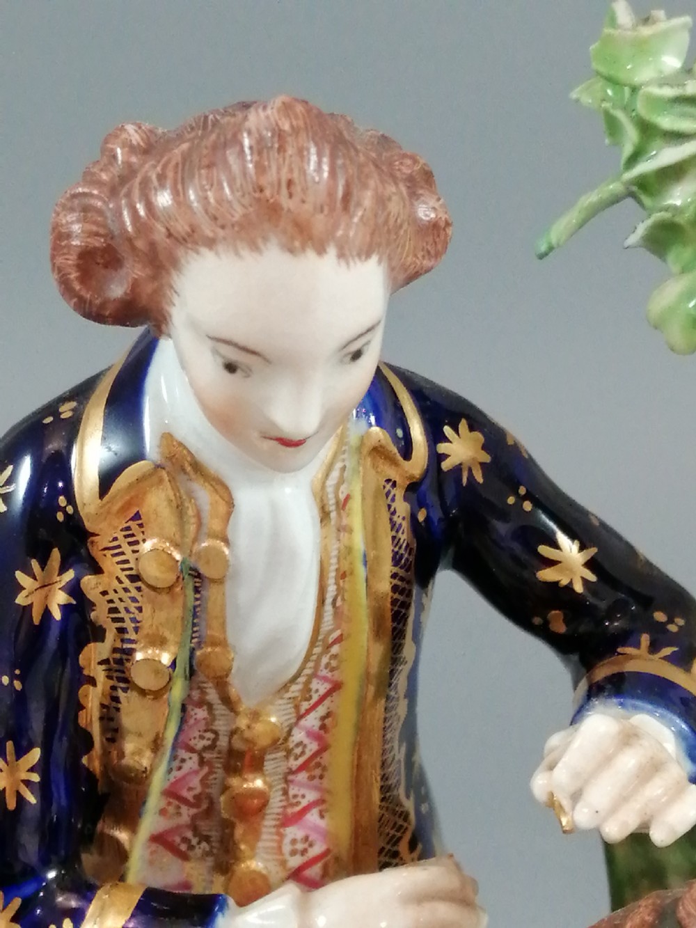 An early nineteenth-century painted porcelain figurine depicting a male court hairdresser styling a seated ladys hair on a rococo scroll base. View XIII
