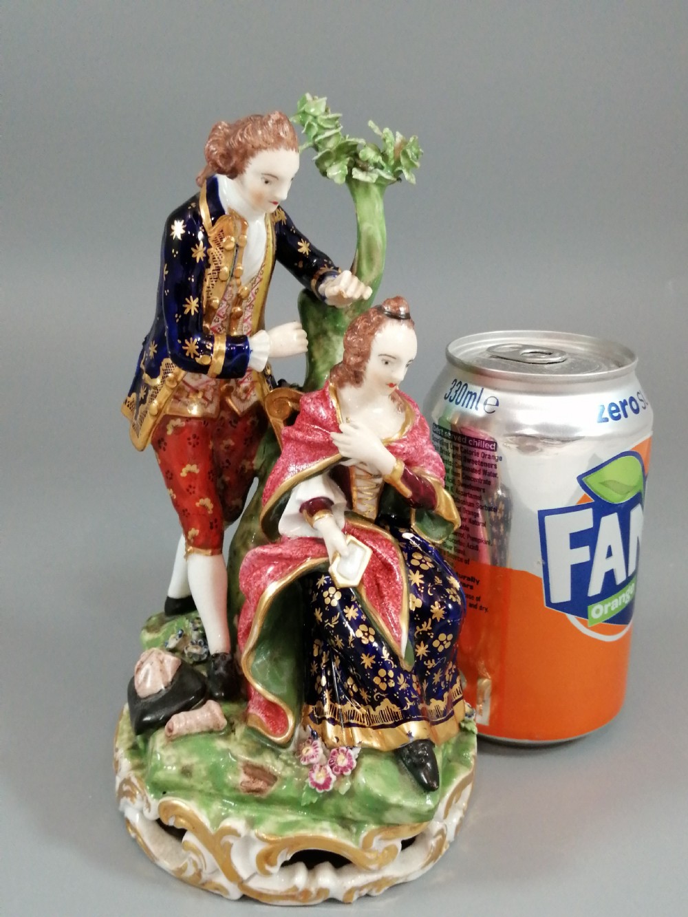 An early nineteenth-century painted porcelain figurine depicting a male court hairdresser styling a seated ladys hair on a rococo scroll base. View XVI