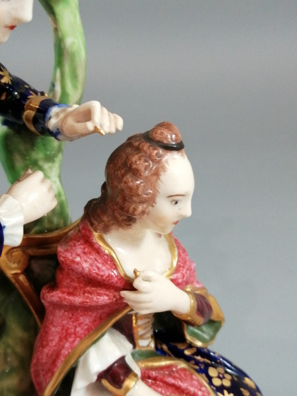 An early nineteenth-century painted porcelain figurine depicting a male court hairdresser styling a seated ladys hair on a rococo scroll base. View XVII