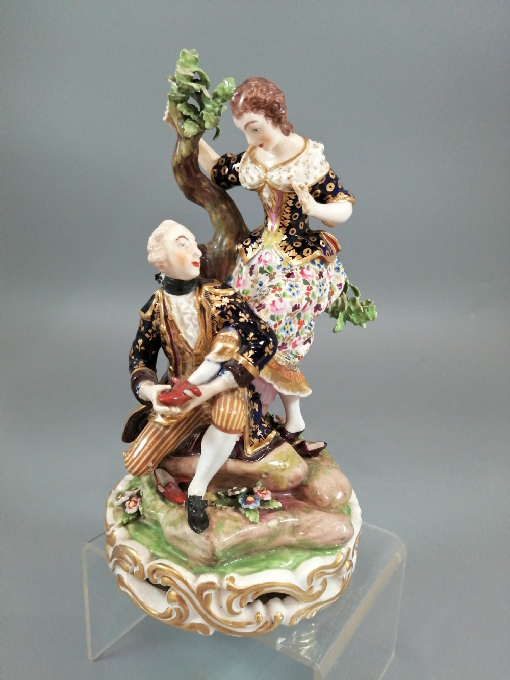 Early 19th-century Derby porcelain figural group depicting a shoemaker and a standing lady beside a tree on a gilded scroll base.