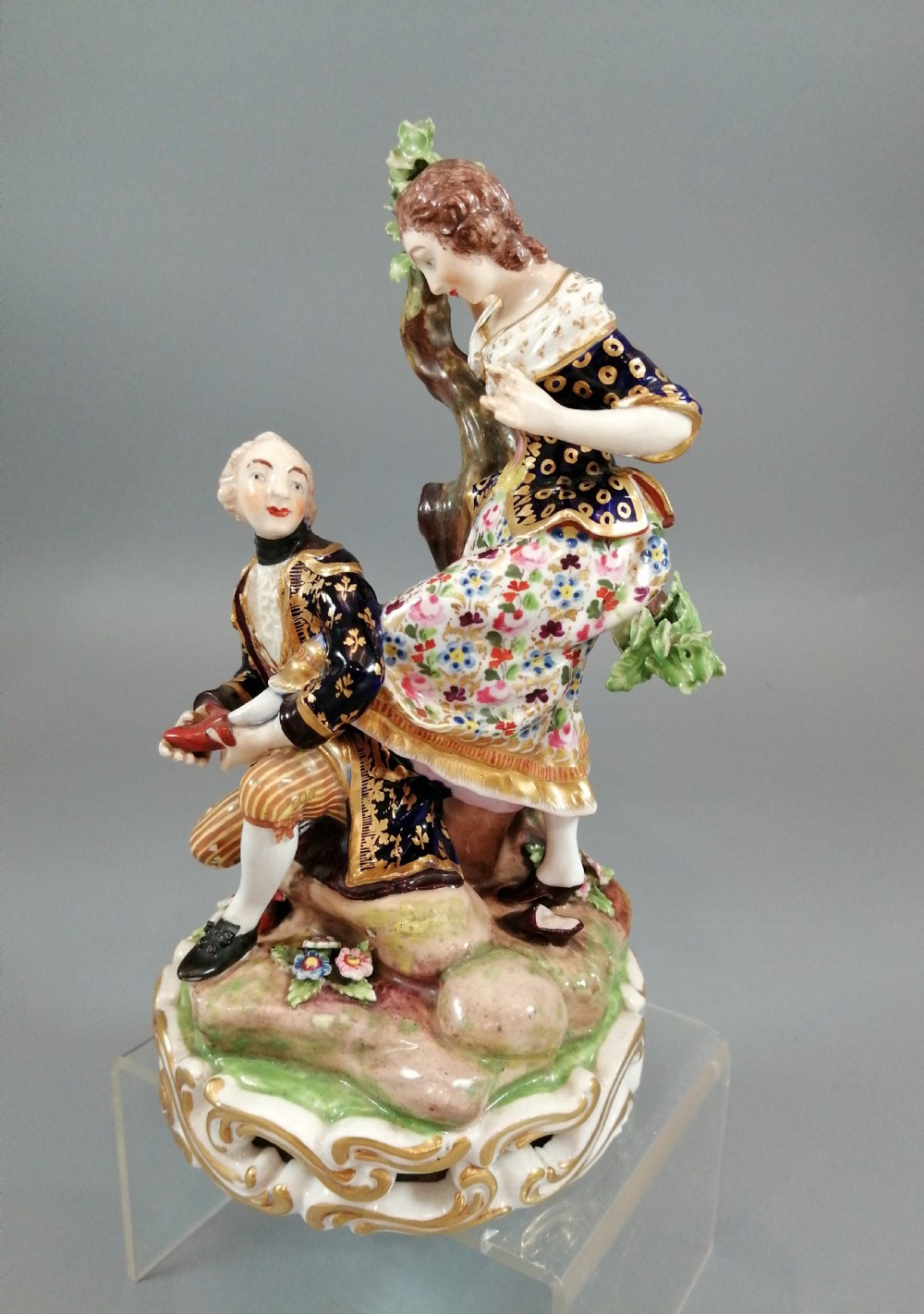Early 19th-century Derby porcelain figural group depicting a shoemaker and a standing lady beside a tree on a gilded scroll base. View II