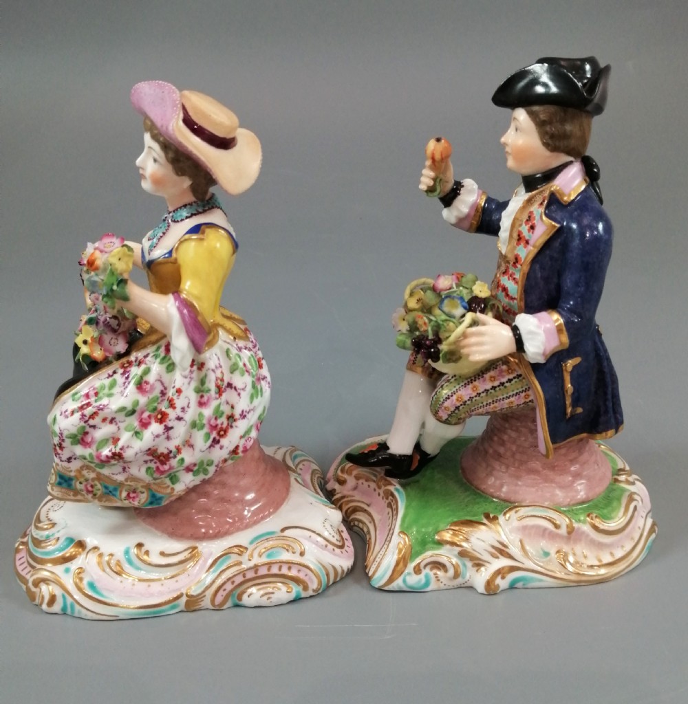 Pair of hand-painted porcelain figurines depicting a male and female gardener seated on Rococo scrolling bases adorned with encrusted flowers. View II