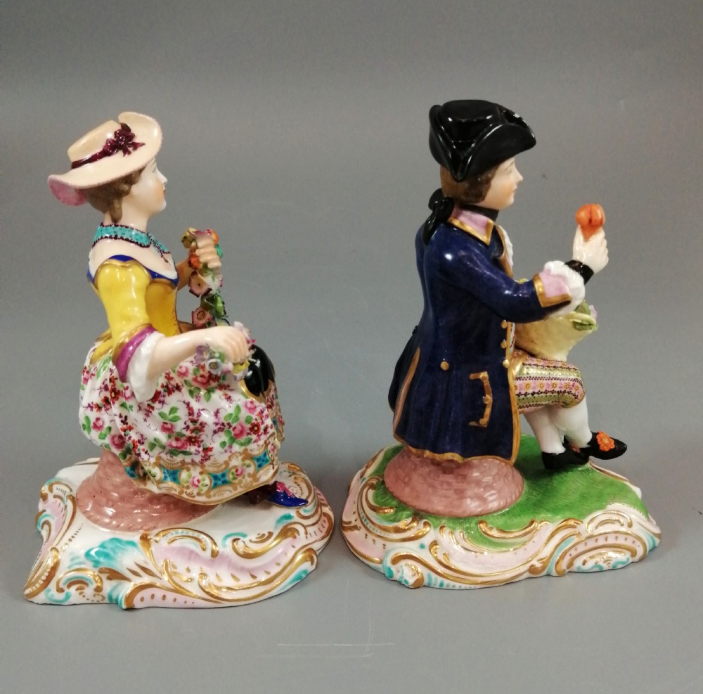 Pair of hand-painted porcelain figurines depicting a male and female gardener seated on Rococo scrolling bases adorned with encrusted flowers. View V