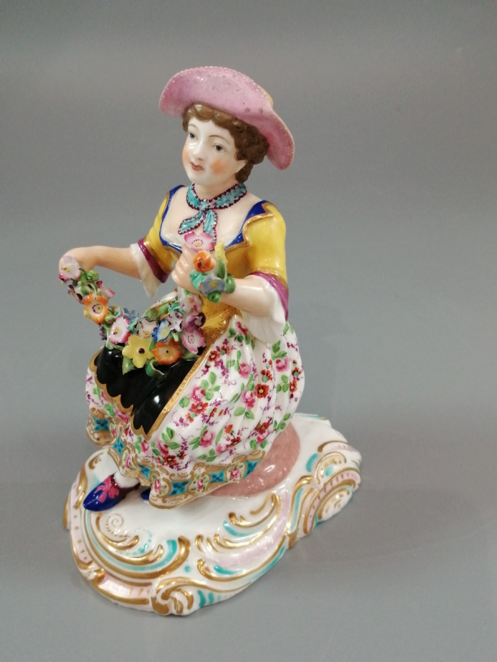 Pair of hand-painted porcelain figurines depicting a male and female gardener seated on Rococo scrolling bases adorned with encrusted flowers. View IX