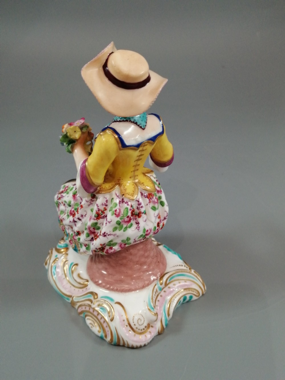 Pair of hand-painted porcelain figurines depicting a male and female gardener seated on Rococo scrolling bases adorned with encrusted flowers. View X