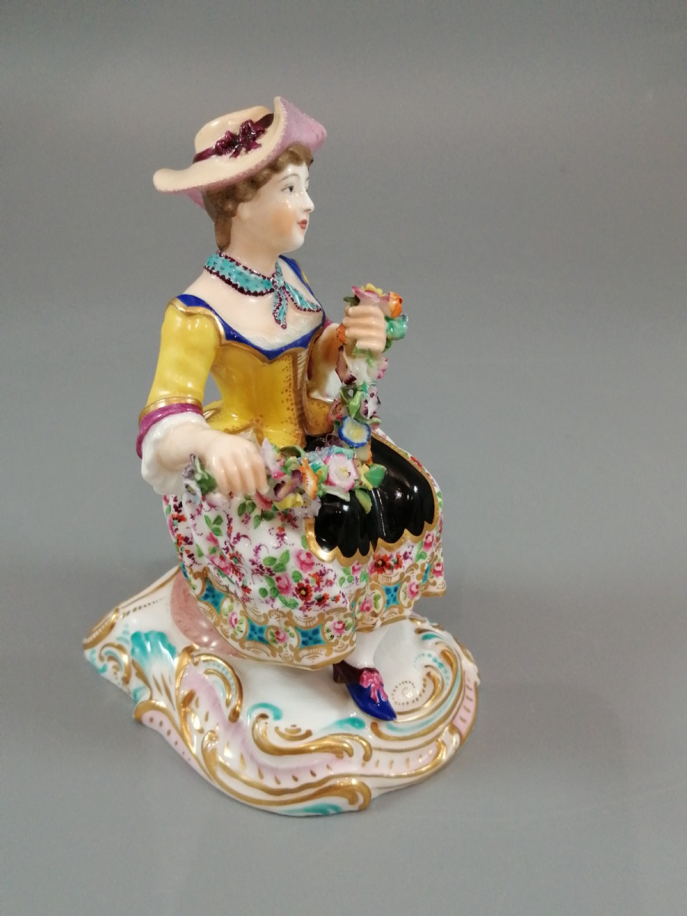 Pair of hand-painted porcelain figurines depicting a male and female gardener seated on Rococo scrolling bases adorned with encrusted flowers. View XII