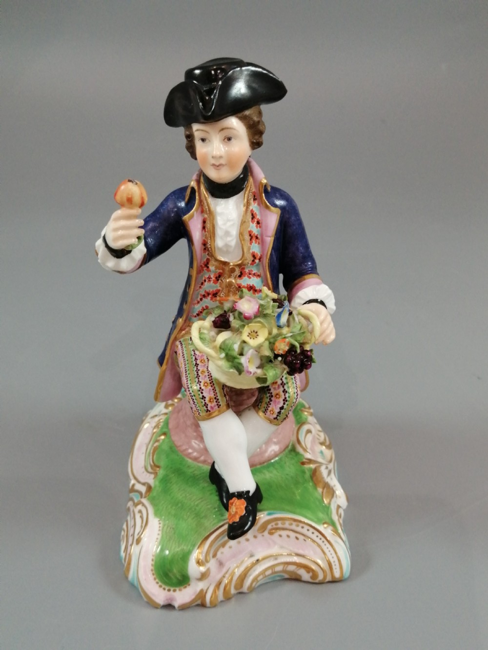 Pair of hand-painted porcelain figurines depicting a male and female gardener seated on Rococo scrolling bases adorned with encrusted flowers. View XIV