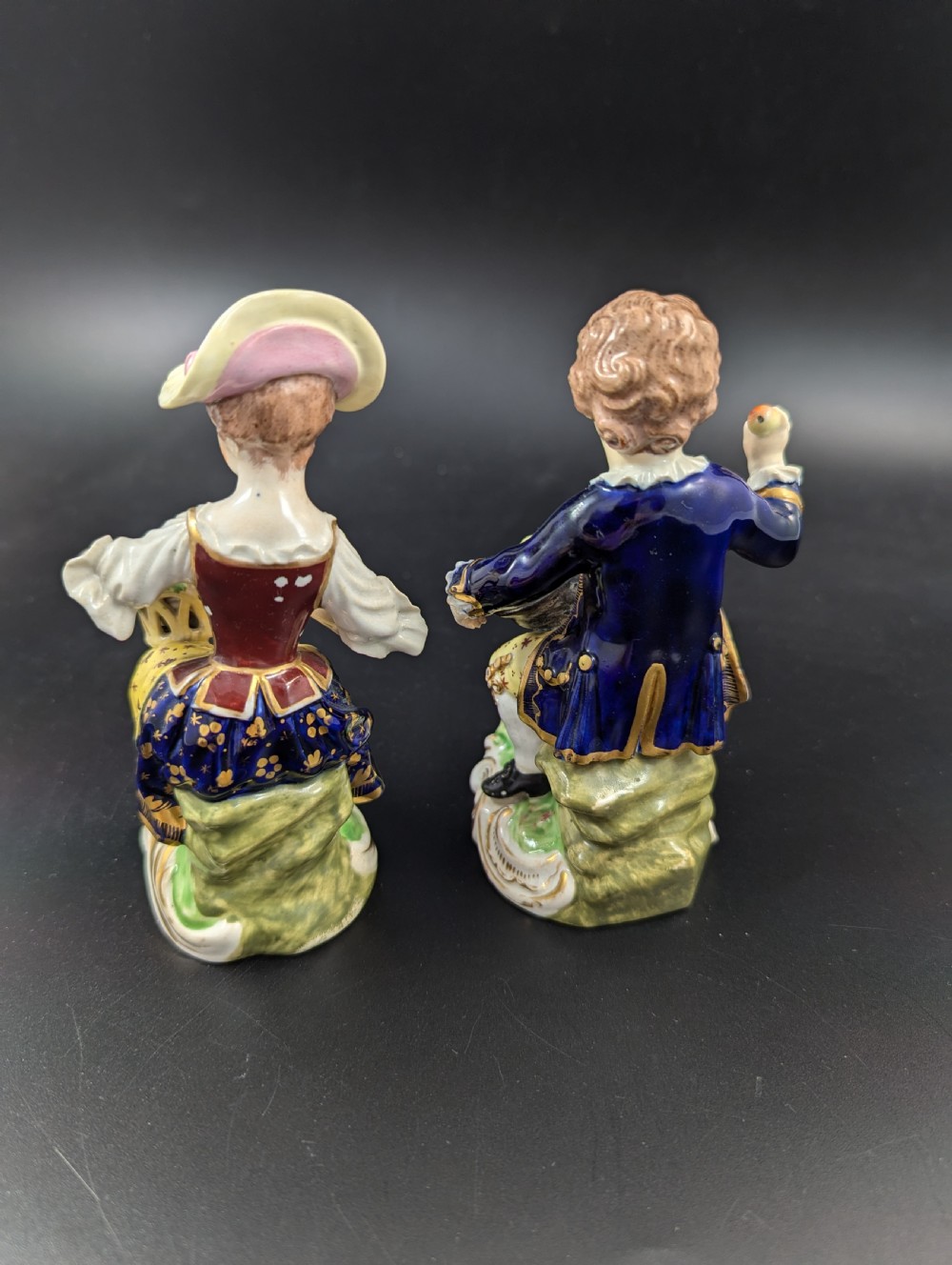 A pair of antique hand-painted Derby porcelain figurines featuring a young female gardener with a basket of flowers and a male gardener holding fruit on gilt scroll bases. View III