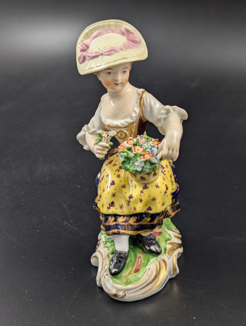 A pair of antique hand-painted Derby porcelain figurines featuring a young female gardener with a basket of flowers and a male gardener holding fruit on gilt scroll bases. View VI