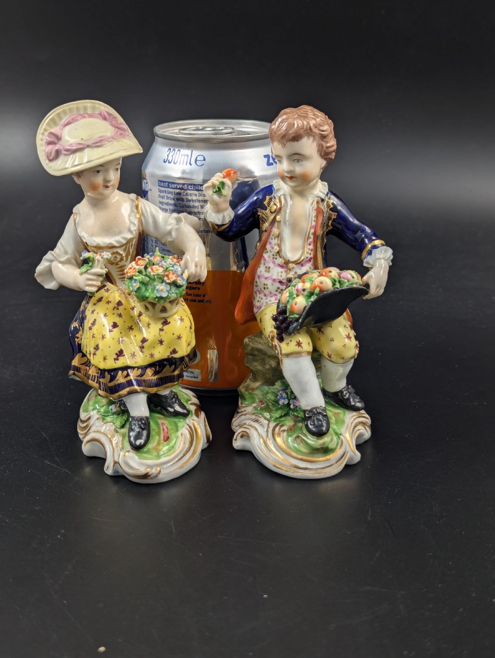 A pair of antique hand-painted Derby porcelain figurines featuring a young female gardener with a basket of flowers and a male gardener holding fruit on gilt scroll bases. View VII