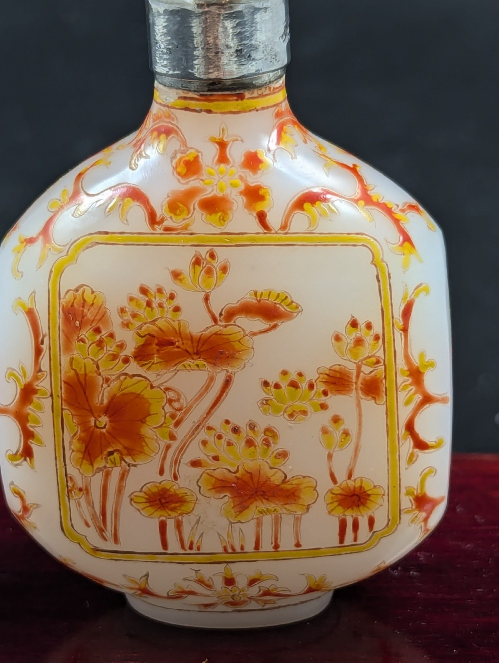 An opaque white glass snuff bottle featuring orange lotus enamel decoration within a central panel and a silver-tone spherical stopper. View II