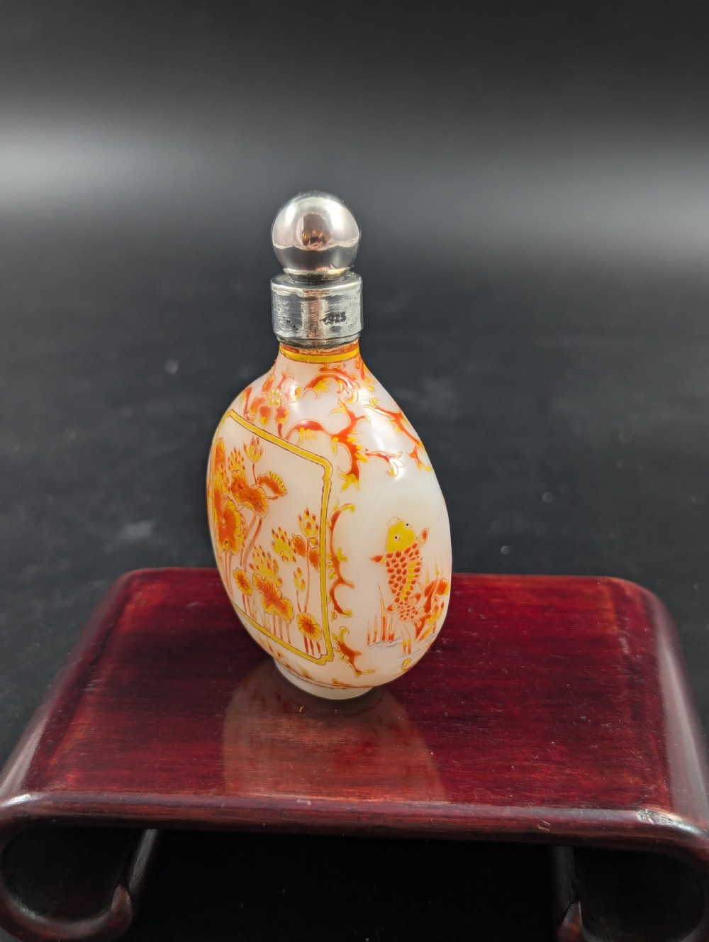An opaque white glass snuff bottle featuring orange lotus enamel decoration within a central panel and a silver-tone spherical stopper. View III