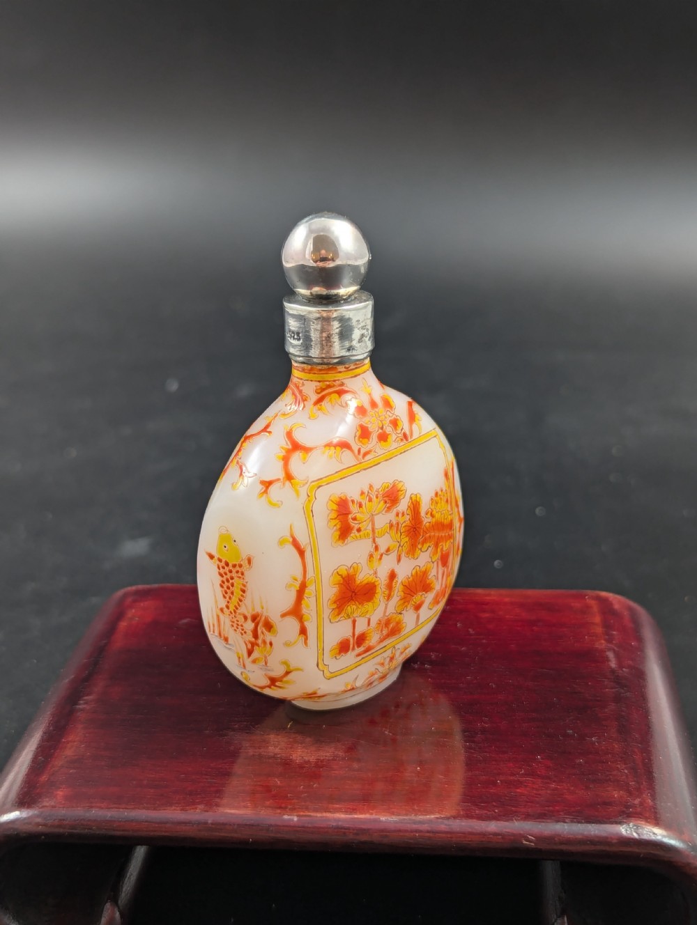 An opaque white glass snuff bottle featuring orange lotus enamel decoration within a central panel and a silver-tone spherical stopper. View IV