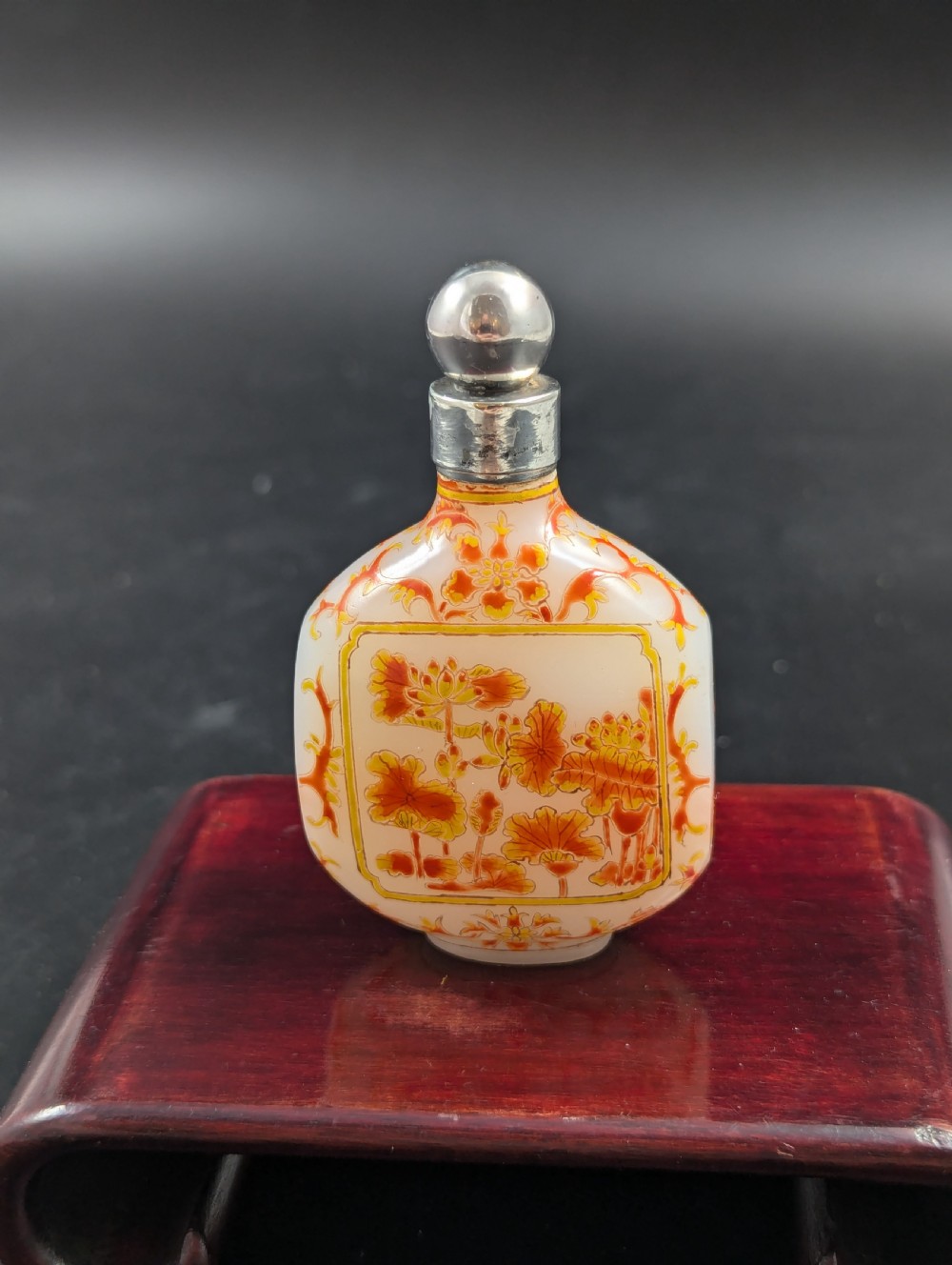 An opaque white glass snuff bottle featuring orange lotus enamel decoration within a central panel and a silver-tone spherical stopper. View V