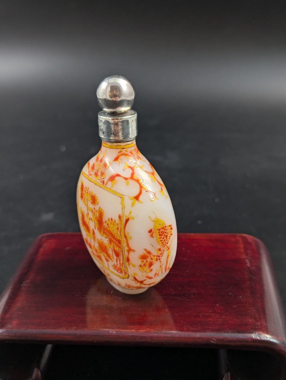 An opaque white glass snuff bottle featuring orange lotus enamel decoration within a central panel and a silver-tone spherical stopper. View VI