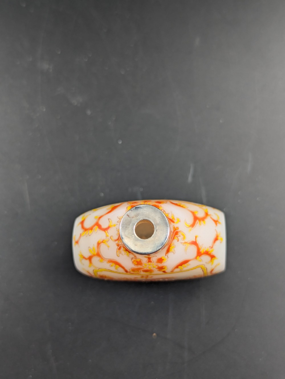 An opaque white glass snuff bottle featuring orange lotus enamel decoration within a central panel and a silver-tone spherical stopper. View IX