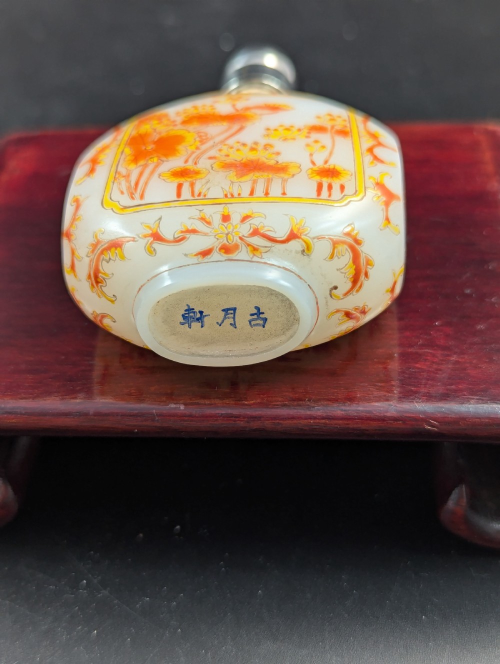 An opaque white glass snuff bottle featuring orange lotus enamel decoration within a central panel and a silver-tone spherical stopper. View X