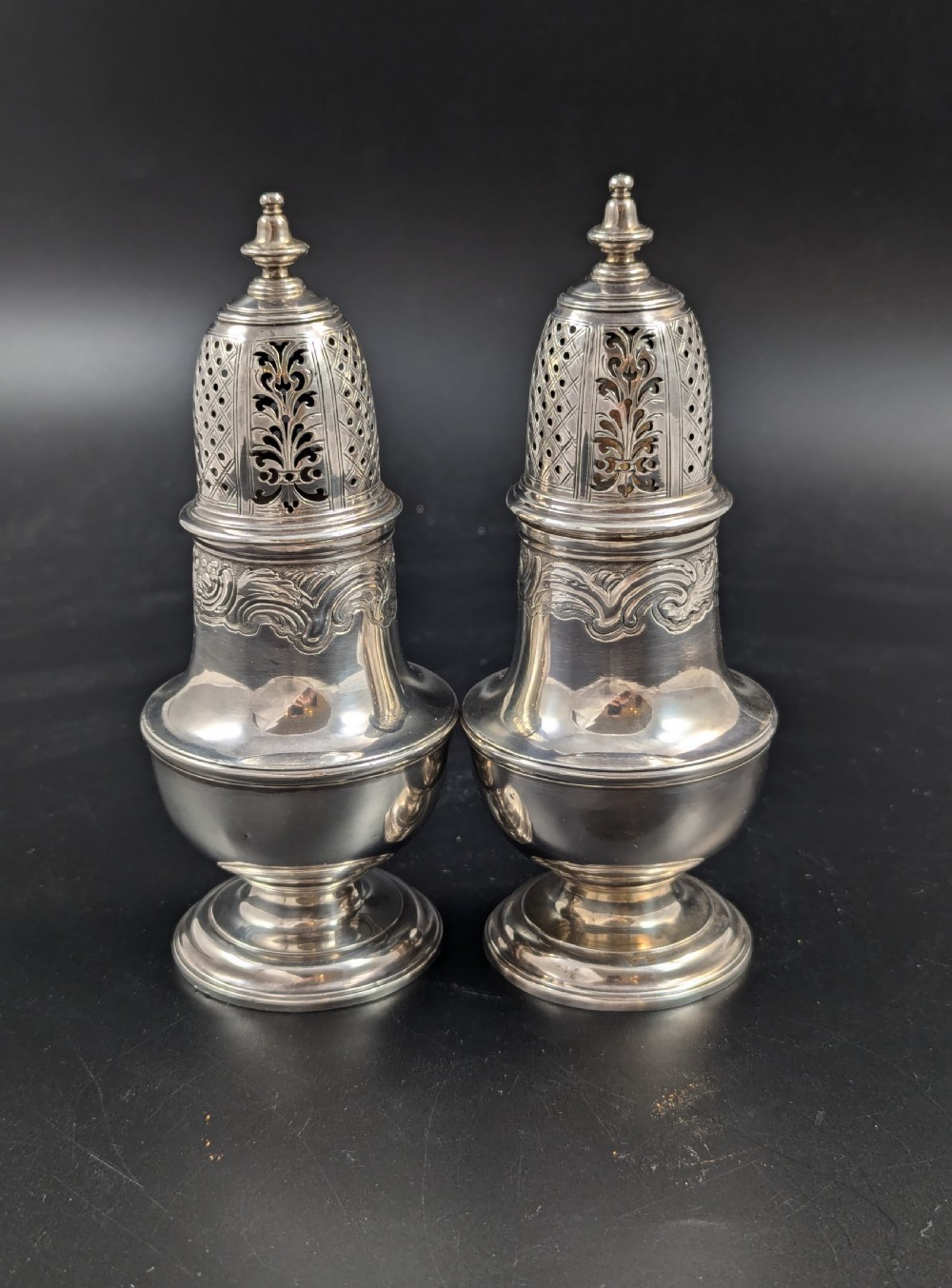 A pair of George II sterling silver baluster-form casters featuring pierced lattice tops, chased scroll detailing, and stepped pedestal bases. View IV