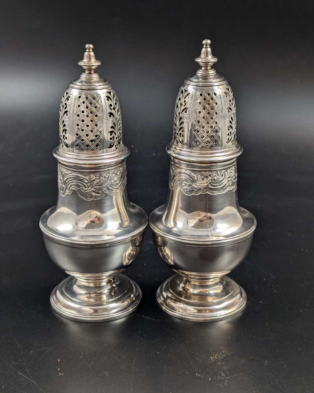 A pair of George II sterling silver baluster-form casters featuring pierced lattice tops, chased scroll detailing, and stepped pedestal bases. View VI