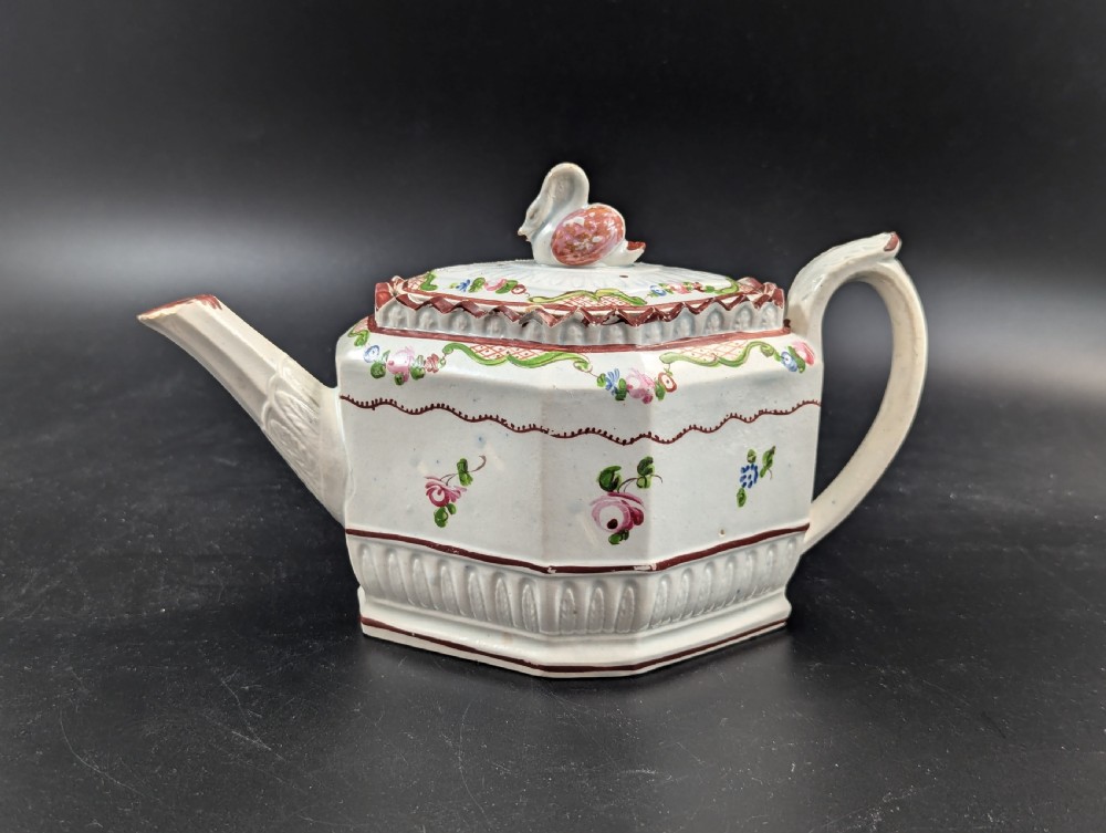 An octagonal off-white antique pearlware teapot decorated with hand-painted floral sprigs, a fluted base, and a swan-form lid knop.