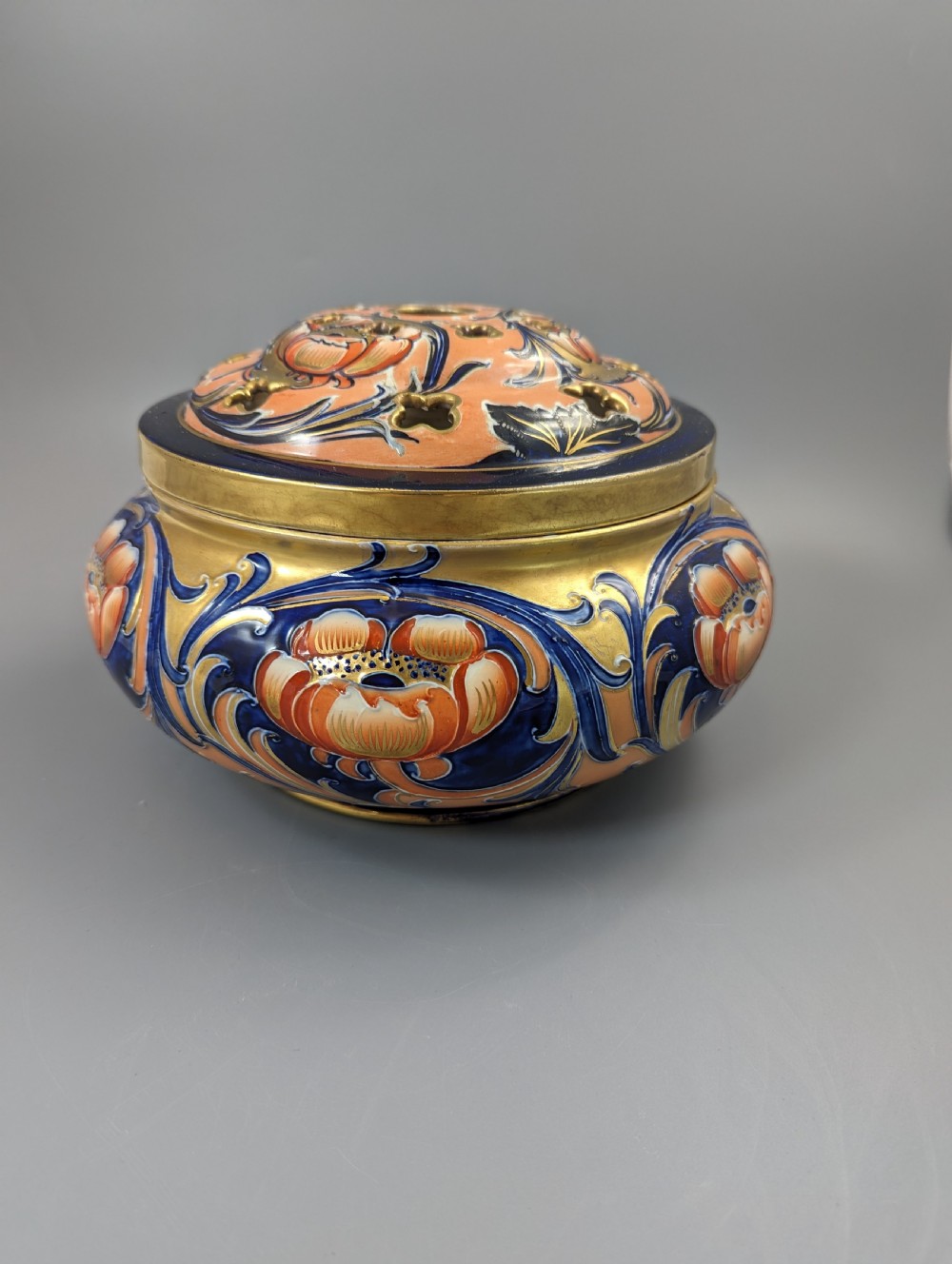 An Edwardian Moorcroft Macintyre ceramic pot pourri jar with a pierced lid, featuring hand-painted tube-lined floral decoration in cobalt blue, coral, and gold.