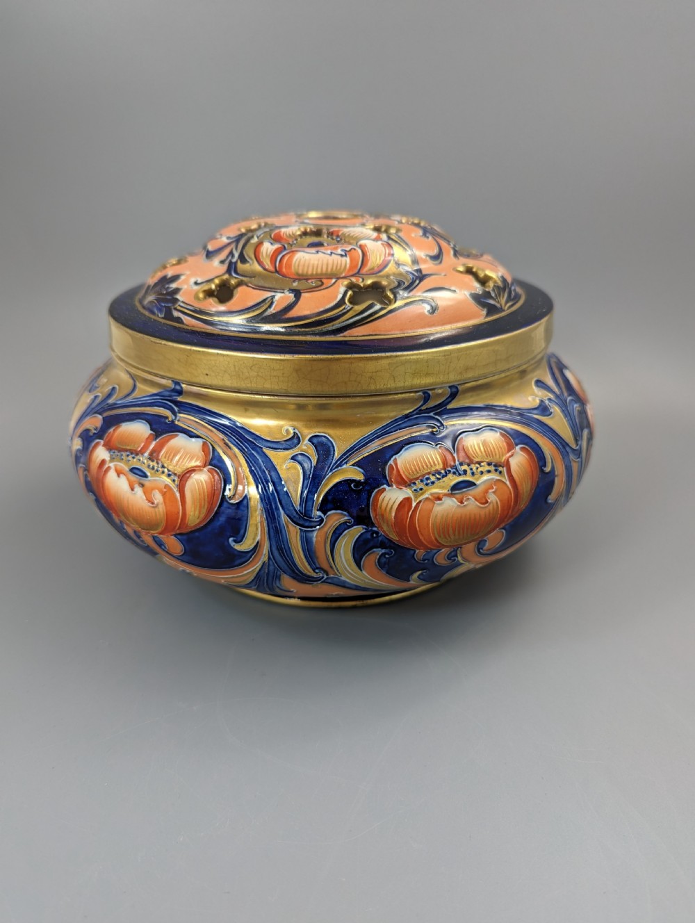 An Edwardian Moorcroft Macintyre ceramic pot pourri jar with a pierced lid, featuring hand-painted tube-lined floral decoration in cobalt blue, coral, and gold. View V