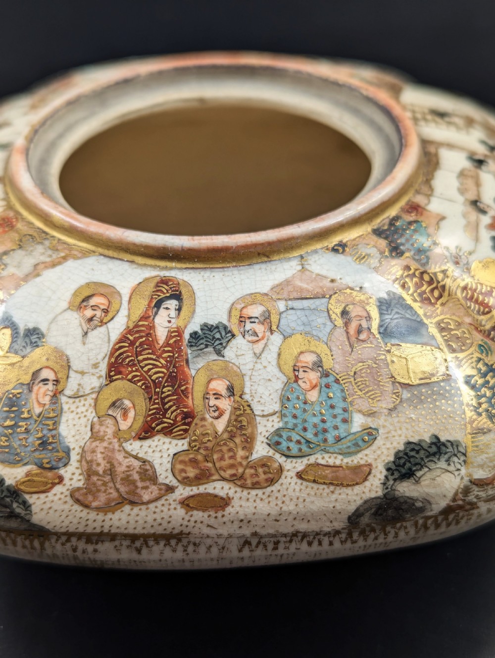 A squarish, lobed Satsuma earthenware vessel featuring hand-painted figures with gold halos, elaborate gilded borders, and a crackled ivory glaze. View II