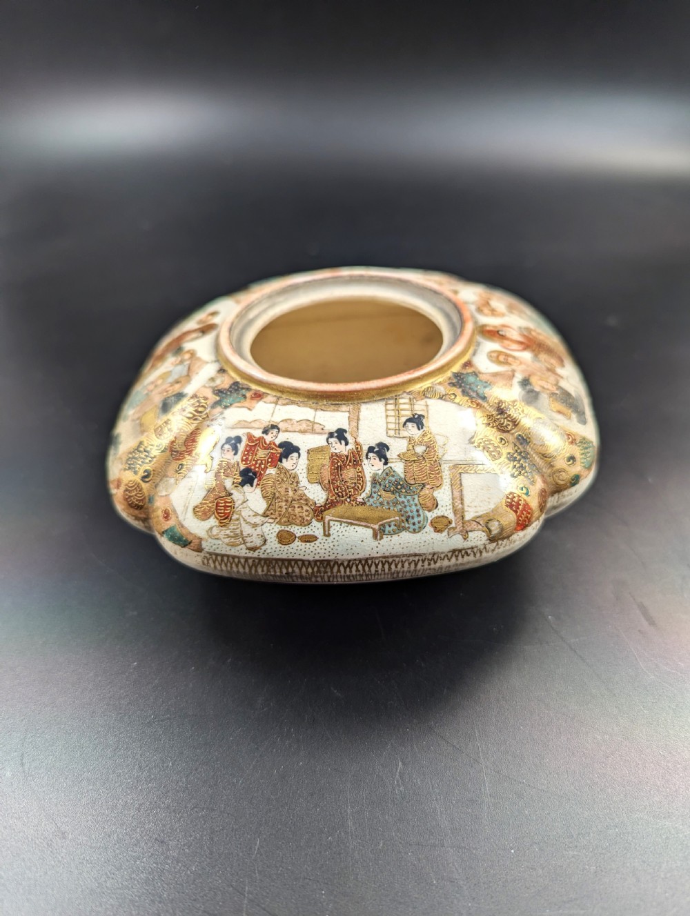 A squarish, lobed Satsuma earthenware vessel featuring hand-painted figures with gold halos, elaborate gilded borders, and a crackled ivory glaze. View IV