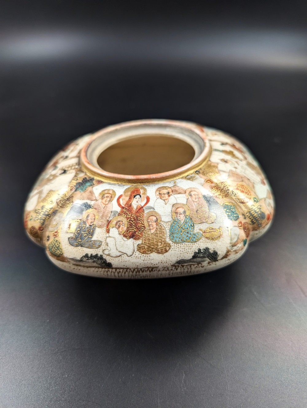 A squarish, lobed Satsuma earthenware vessel featuring hand-painted figures with gold halos, elaborate gilded borders, and a crackled ivory glaze. View V