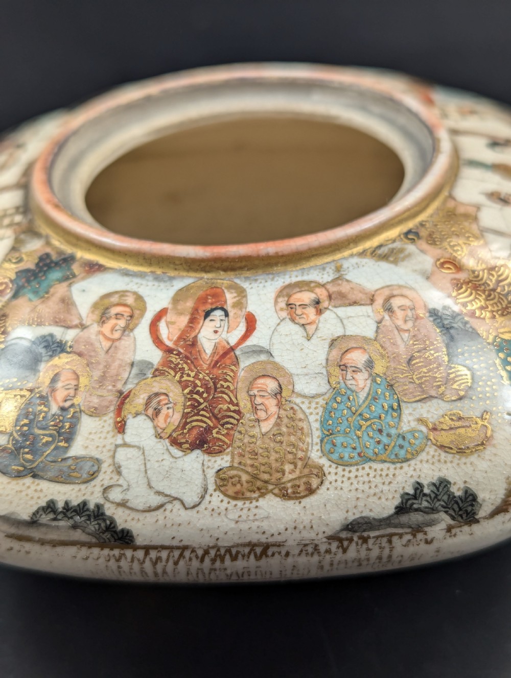 A squarish, lobed Satsuma earthenware vessel featuring hand-painted figures with gold halos, elaborate gilded borders, and a crackled ivory glaze. View VI