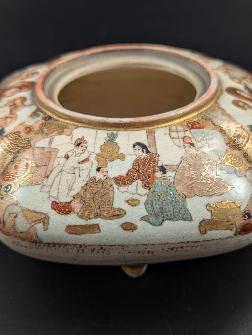 A squarish, lobed Satsuma earthenware vessel featuring hand-painted figures with gold halos, elaborate gilded borders, and a crackled ivory glaze. View VII