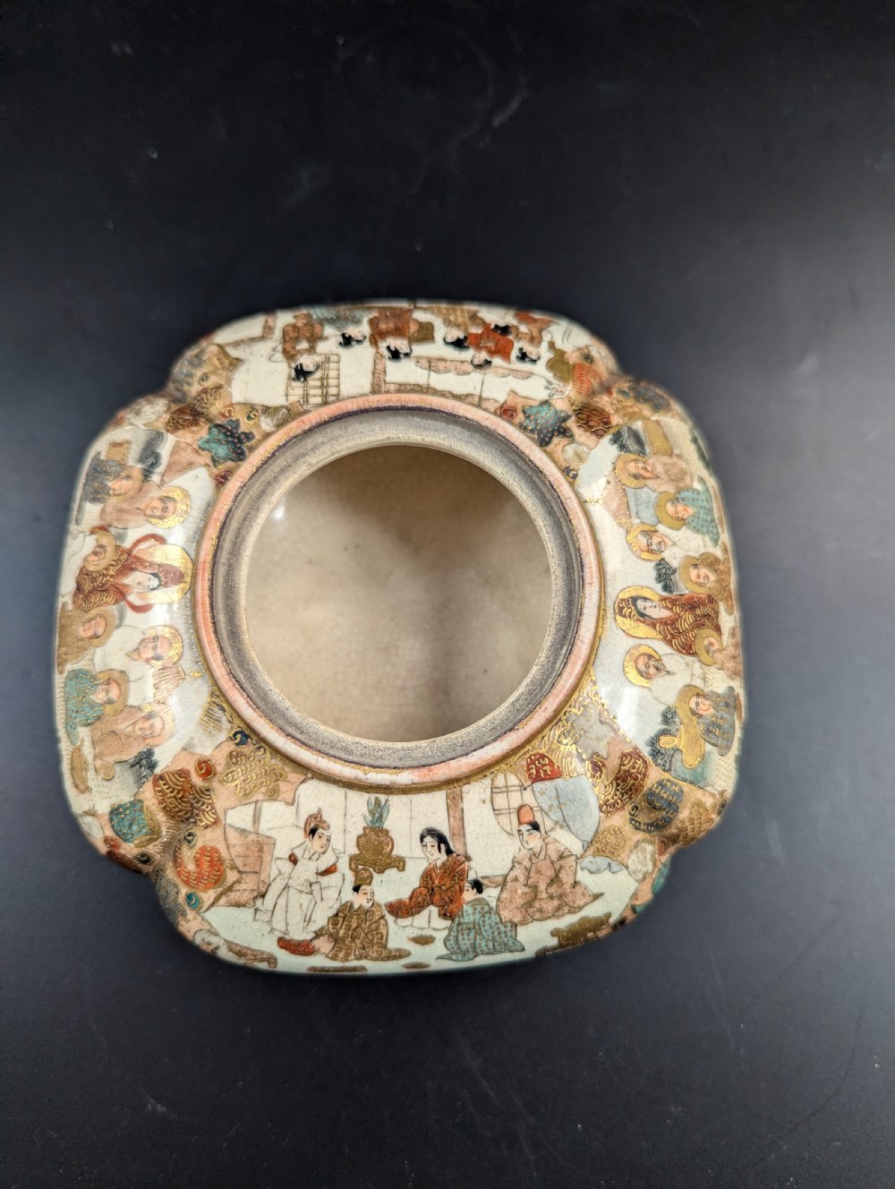 A squarish, lobed Satsuma earthenware vessel featuring hand-painted figures with gold halos, elaborate gilded borders, and a crackled ivory glaze. View IX