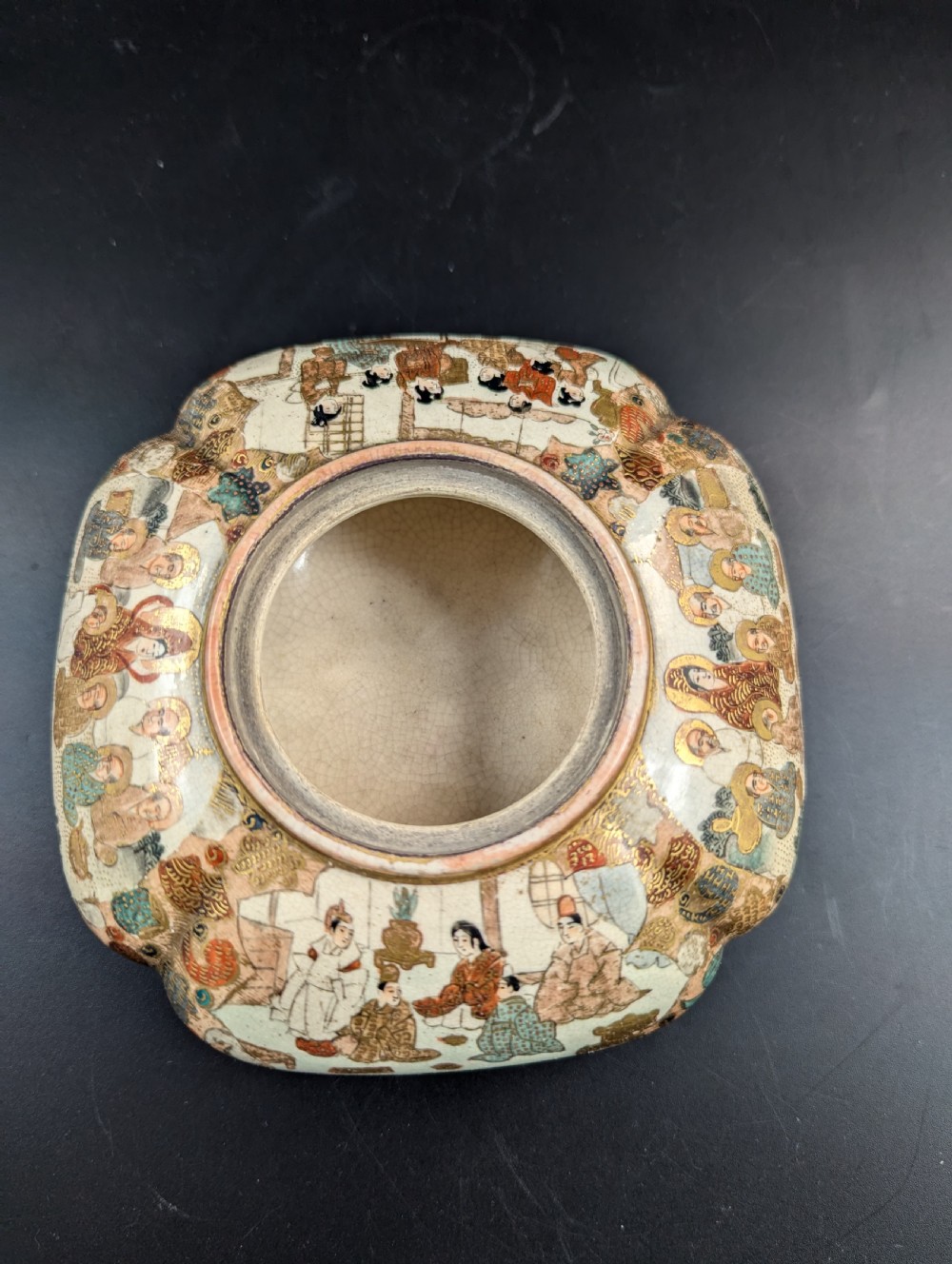 A squarish, lobed Satsuma earthenware vessel featuring hand-painted figures with gold halos, elaborate gilded borders, and a crackled ivory glaze. View X