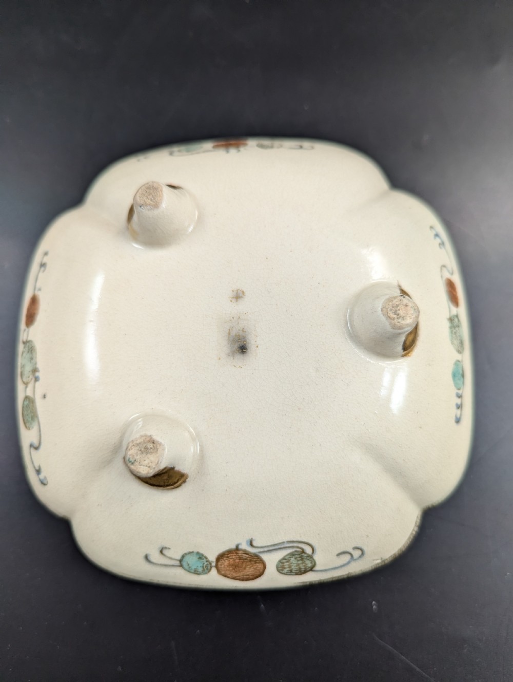 A squarish, lobed Satsuma earthenware vessel featuring hand-painted figures with gold halos, elaborate gilded borders, and a crackled ivory glaze. View XI