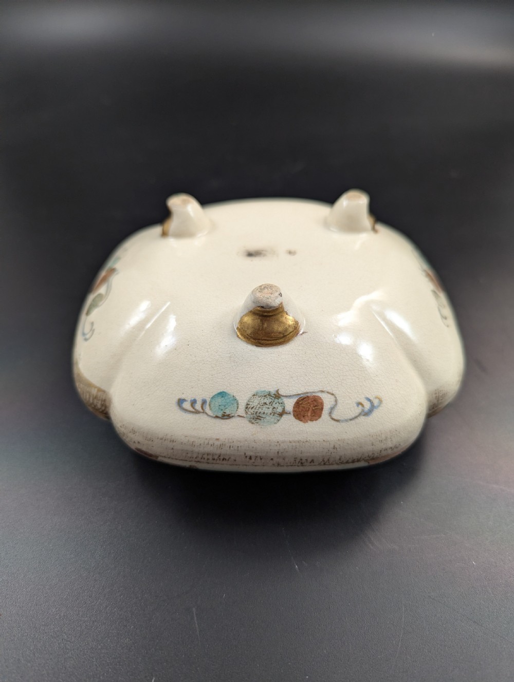 A squarish, lobed Satsuma earthenware vessel featuring hand-painted figures with gold halos, elaborate gilded borders, and a crackled ivory glaze. View XII