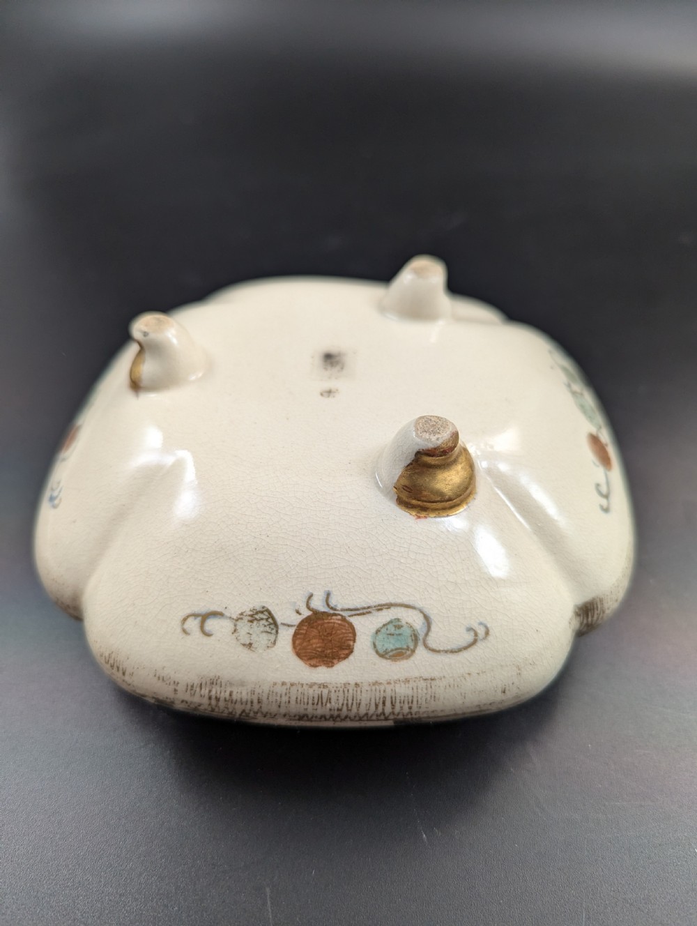 A squarish, lobed Satsuma earthenware vessel featuring hand-painted figures with gold halos, elaborate gilded borders, and a crackled ivory glaze. View XIII