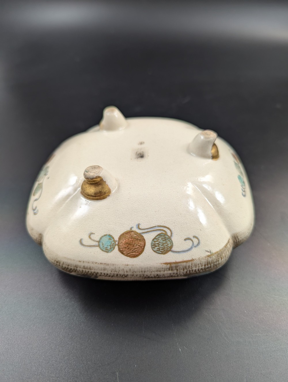 A squarish, lobed Satsuma earthenware vessel featuring hand-painted figures with gold halos, elaborate gilded borders, and a crackled ivory glaze. View XV