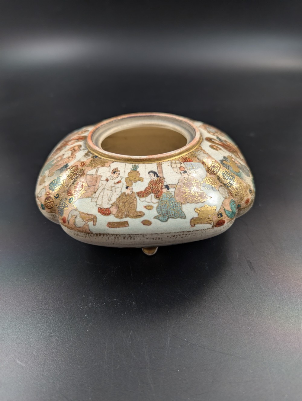 A squarish, lobed Satsuma earthenware vessel featuring hand-painted figures with gold halos, elaborate gilded borders, and a crackled ivory glaze. View XVI