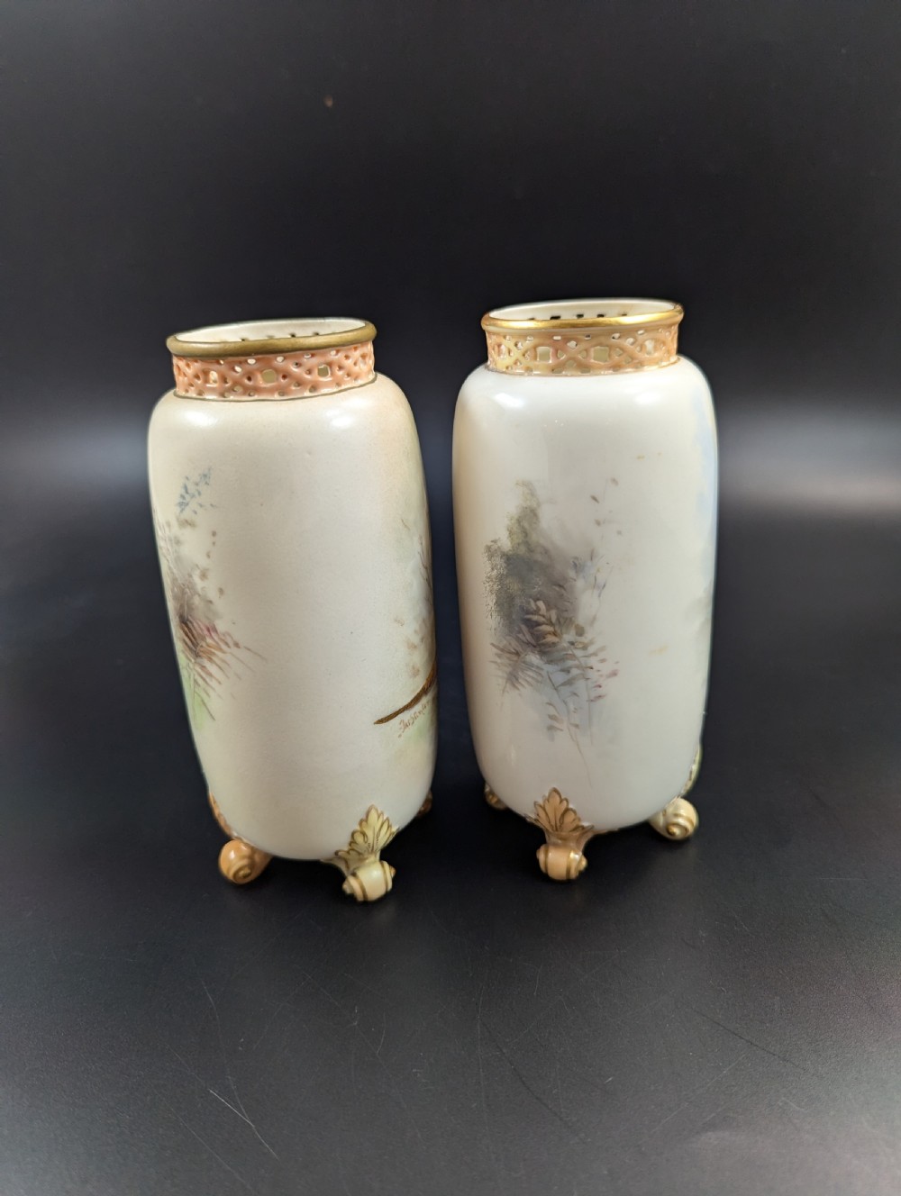 A pair of Edwardian Royal Worcester porcelain vases featuring hand-painted pheasants in natural landscapes, with reticulated rims and gilt scroll feet. View IV