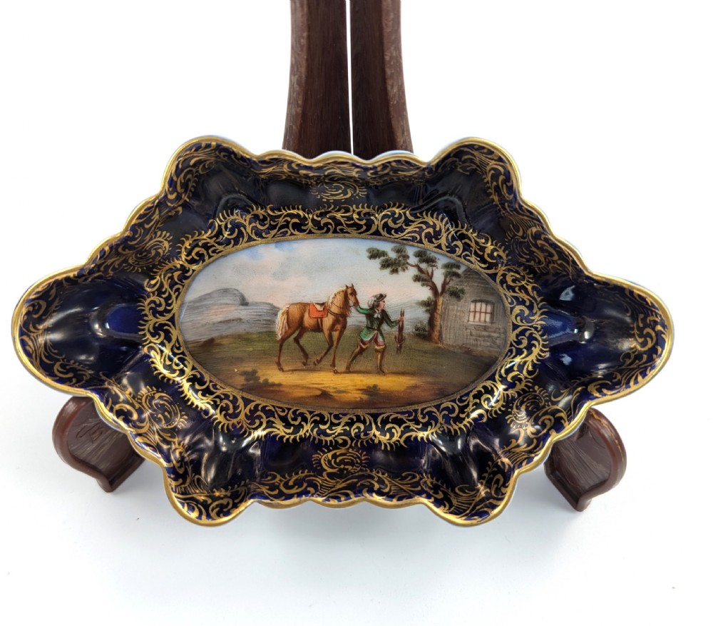 An oval lobed Dresden porcelain dish featuring a cobalt blue rim decorated with gilt scrollwork and a central hand-painted equestrian scene.