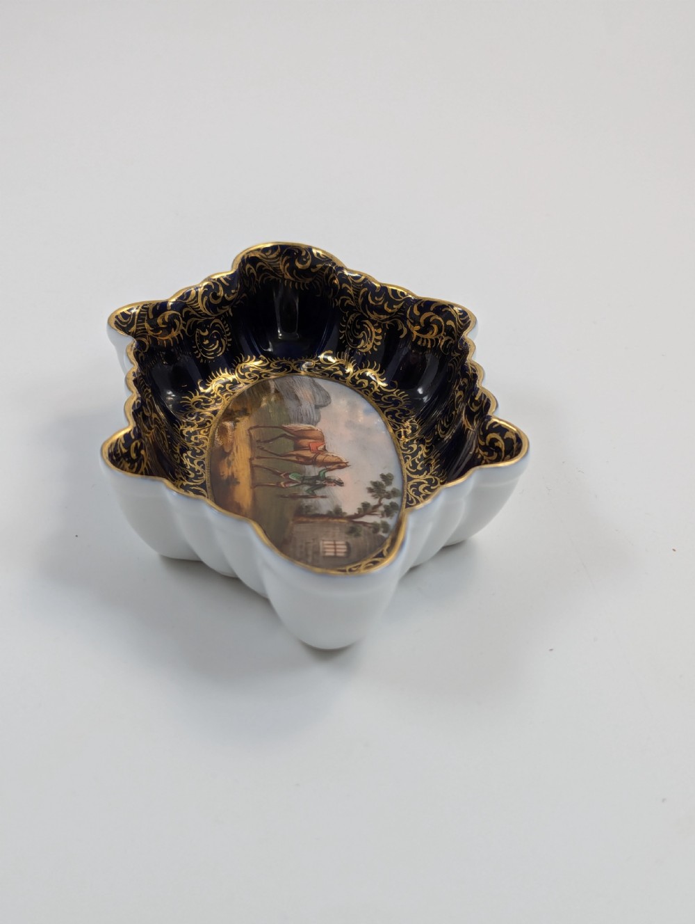 An oval lobed Dresden porcelain dish featuring a cobalt blue rim decorated with gilt scrollwork and a central hand-painted equestrian scene. View IV
