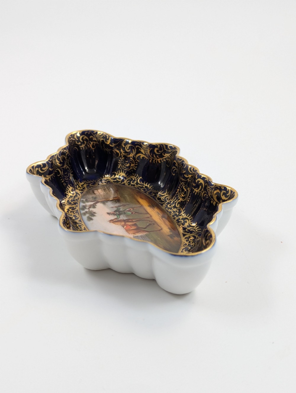 An oval lobed Dresden porcelain dish featuring a cobalt blue rim decorated with gilt scrollwork and a central hand-painted equestrian scene. View VI