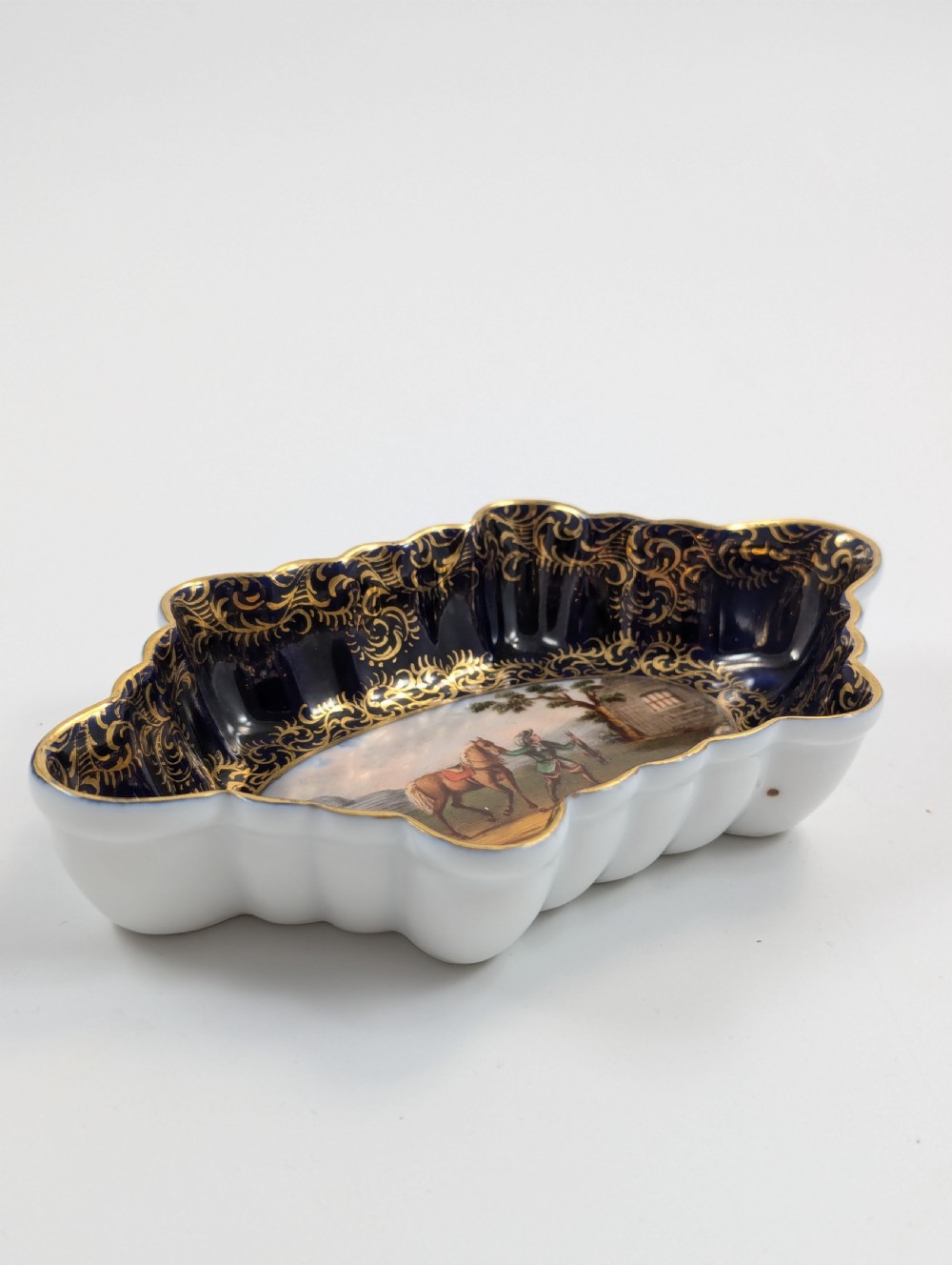 An oval lobed Dresden porcelain dish featuring a cobalt blue rim decorated with gilt scrollwork and a central hand-painted equestrian scene. View VII