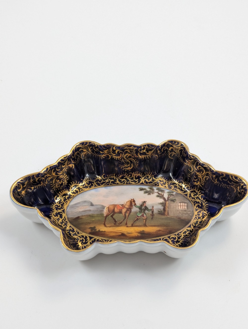An oval lobed Dresden porcelain dish featuring a cobalt blue rim decorated with gilt scrollwork and a central hand-painted equestrian scene. View VIII